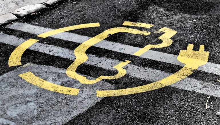 A parking lot with a yellow electric car charging symbol painted on the asphalt.