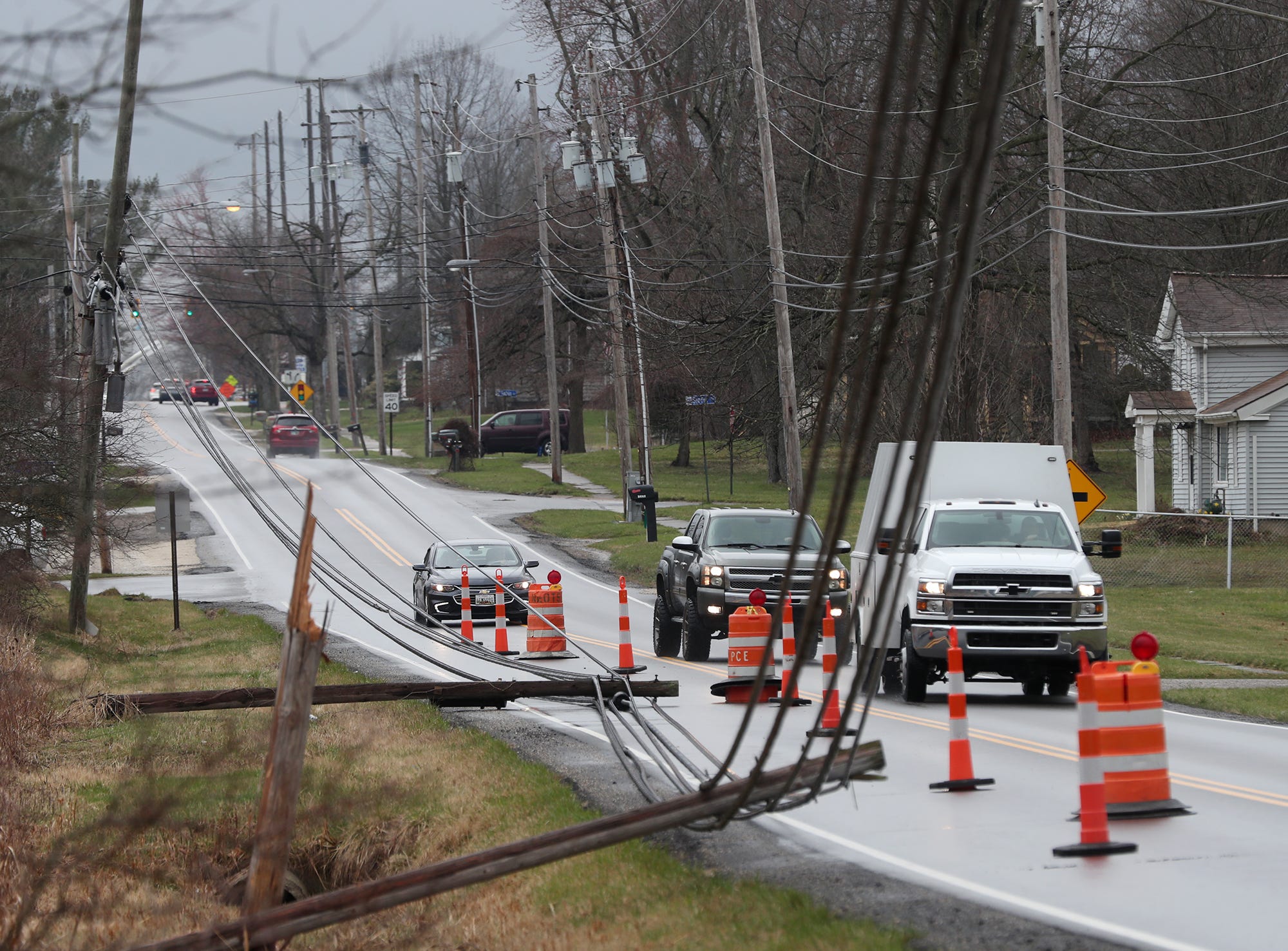 Vehicles traveling eastbound Monday on Tallmadge Road drive past downed utility poles and wires across from Homeland Cemetery in Rootstown.