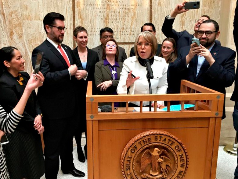 New Mexico Gov. Michelle Lujan Grisham, surrounded by state lawmakers, cabinet officials and others, signs the Energy Transition Act during a ceremony at the State Capitol in Santa Fe on March 22, 2019.